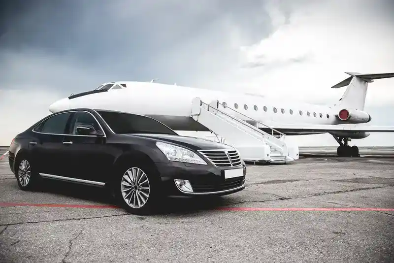 A luxurious black car is parked, waiting for a businessman to disembark from a private jet parked on the tarmac nearby, symbolizing San Antonio Air & Ground Transportation.